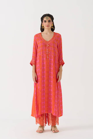 A woman modeling a bright pink and orange kurta set with small gold motifs, standing against a plain white studio background.
